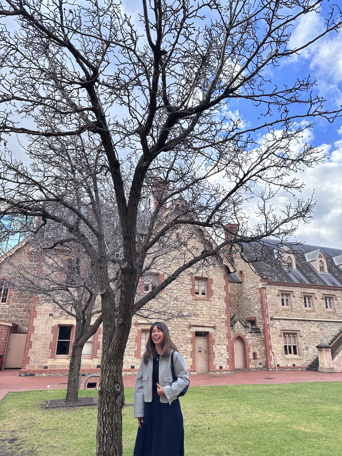 Clarizza smiling beneath a bare tree in front of a sandstone building